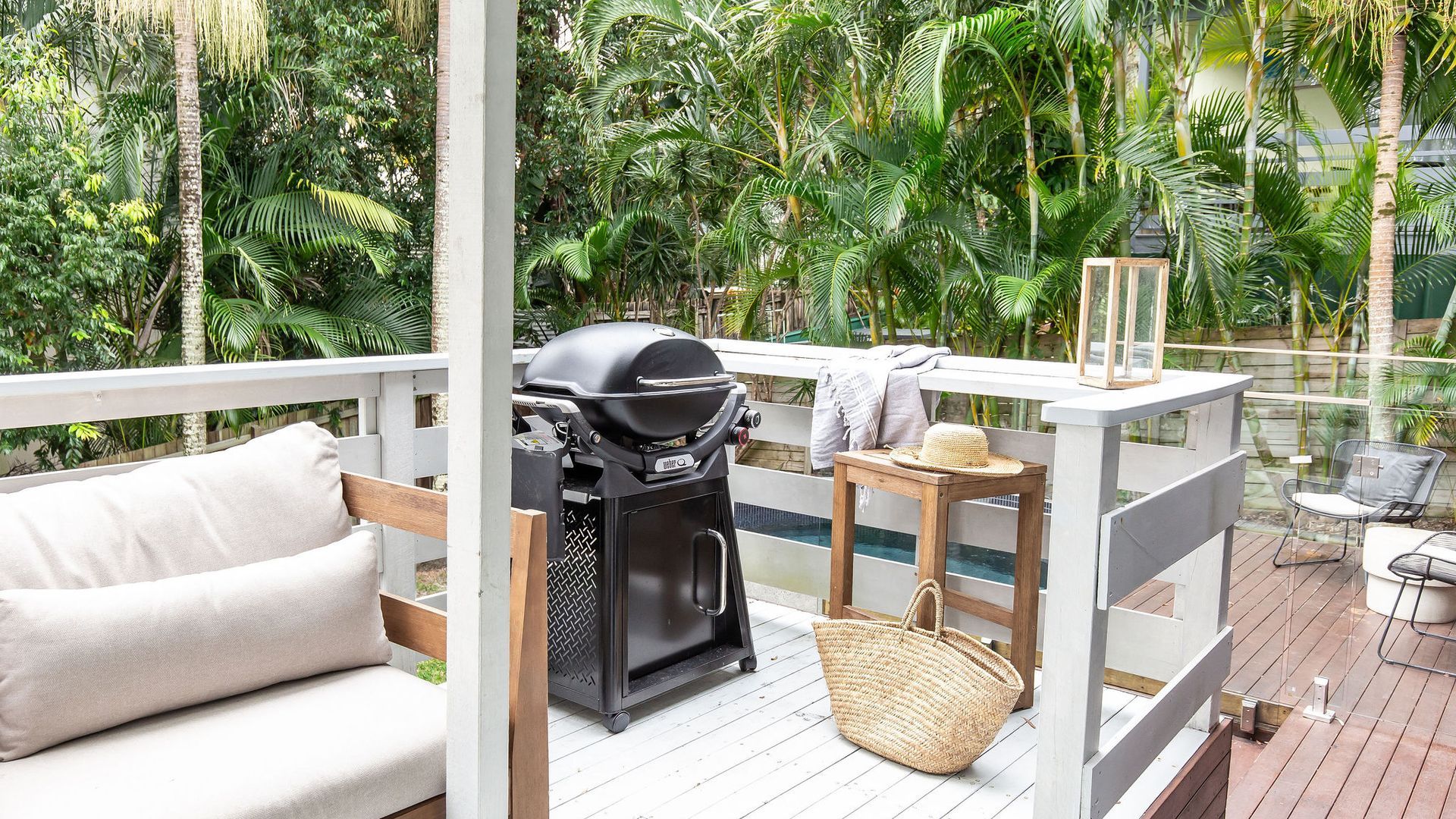 A deck with a grill, seating, and a glass-enclosed pool.