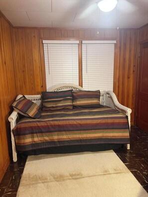 Una habitación con un revestimiento de madera, un sofá blanco tejido con cojines a rayas y una alfombra blanca en el suelo.