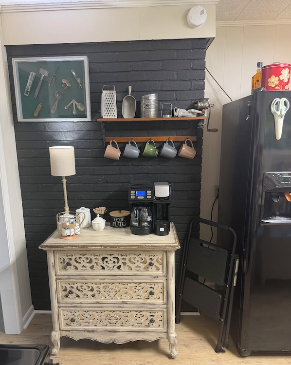 A kitchen with a coffee machine, a decorative cabinet, and a shelf with kitchen utensils.