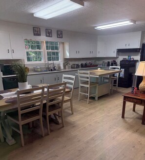 A kitchen with white cabinets, a dining table with chairs, a window with a view of trees, and a refrigerator.