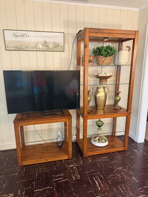 Un moble de televisió de fusta amb un televisor de pantalla plana i un vitrina de vidre amb objectes decoratius.