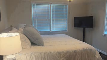 Une chambre à coucher avec un lit, un ventilateur de plafond, une télévision et une fenêtre avec des stores.