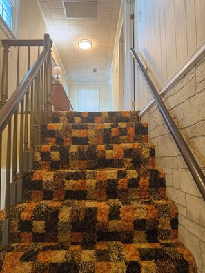 Una escalera con un estampado de alfombra a cuadros, barandillas de madera y una puerta blanca al final.