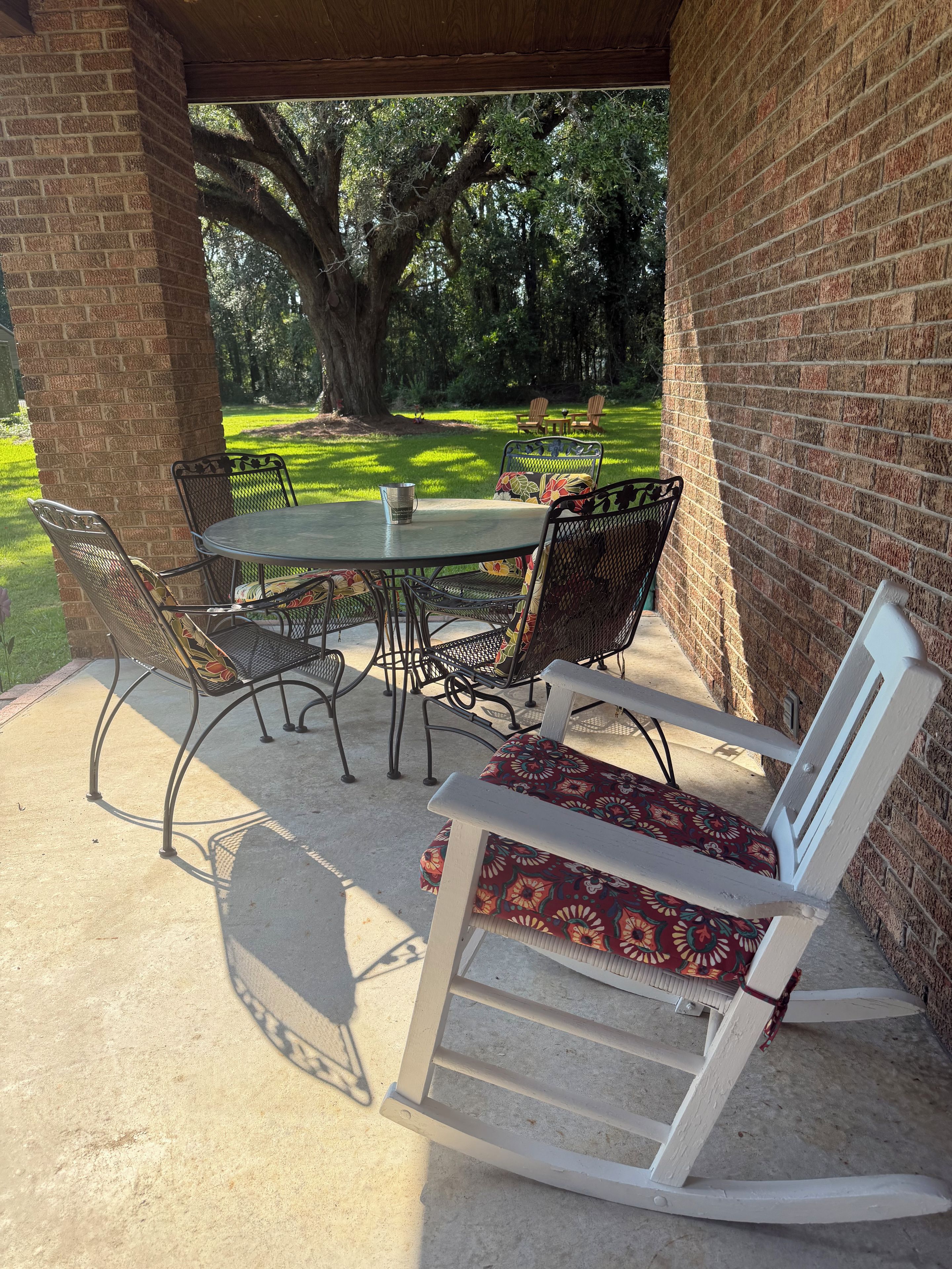 Une terrasse extérieure avec une table et des chaises, un fauteuil à bascule et un mur en briques.