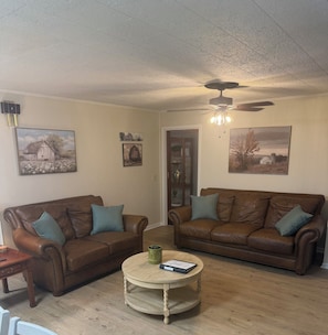 A living room with two brown leather sofas, a round wooden coffee table, and ceiling fans.