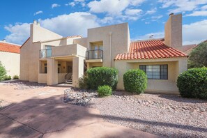 A two-story house with a red-tiled roof, a balcony, and a small garden area with gravel and shrubs. - Dramatic end unit 2 bedrm split floor plan   B26 Great central location (Tucson)