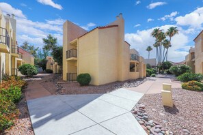 A residential area with multi-story buildings, a paved walkway, and landscaped areas with small shrubs and trees. - Dramatic end unit 2 bedrm split floor plan   B26 Great central location (Tucson)