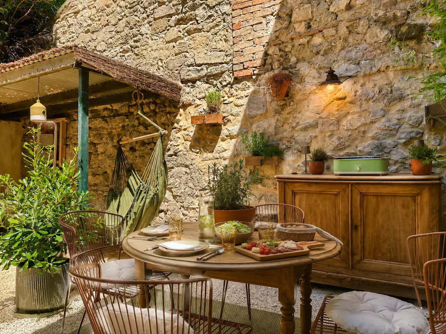 Un espace de restauration extérieur de style rustique, avec un mur en pierre, des meubles en bois et des plantes en pot.