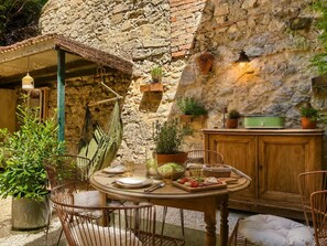 A rustic outdoor dining area with a stone wall, wooden furniture, and potted plants. - Hypercenter • Le Cornue • air-conditioned with a patio (Avignon)