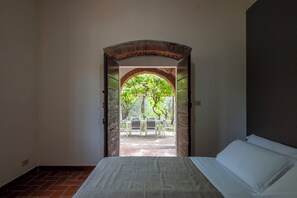 Ein Zimmer mit einem Bett, ein Ziegelbogen, der in einen Außenbereich mit Tisch und Stühlen führt.
