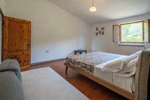 Ein Schlafzimmer mit einem Bett, einem Holzschrank, einem kleinen Tisch, einem Fenster mit Aussicht und einer Hängelampe.