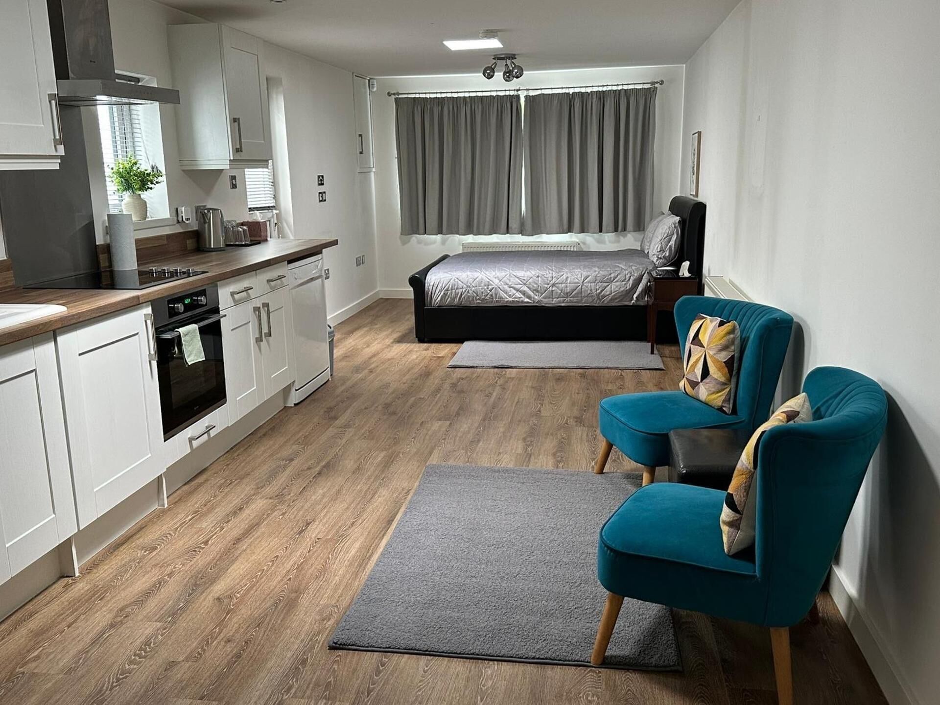 Ein kompaktes Hotelzimmer mit Küchenzeile, einem Bett, einer Sitzecke und Blick ins Freie.