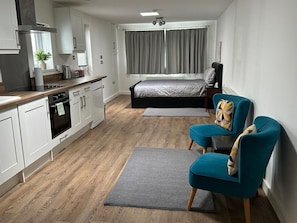 Ein kompaktes Hotelzimmer mit Küchenzeile, einem Bett, einer Sitzecke und Blick ins Freie.