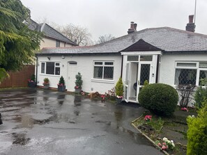 Ein Wohnhaus mit weißer Fassade, einer Veranda und einem Garten mit Blumentöpfen und Blumen.