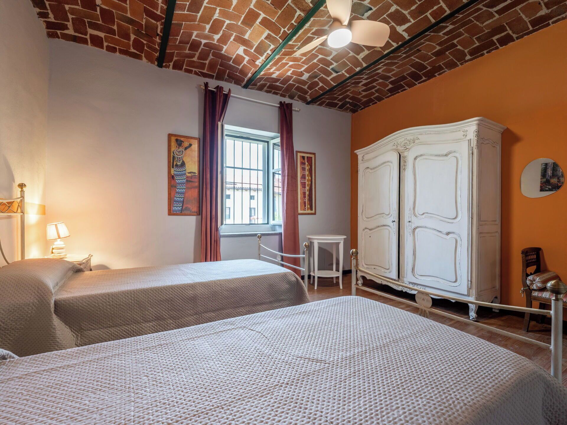 Une chambre avec deux lits, une armoire blanche, une fenêtre avec des rideaux et une petite table.