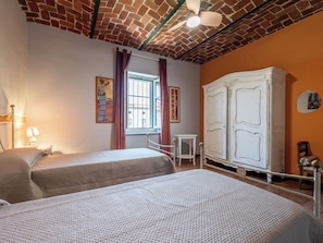 Une chambre avec deux lits, une armoire blanche, une fenêtre avec des rideaux et une petite table.