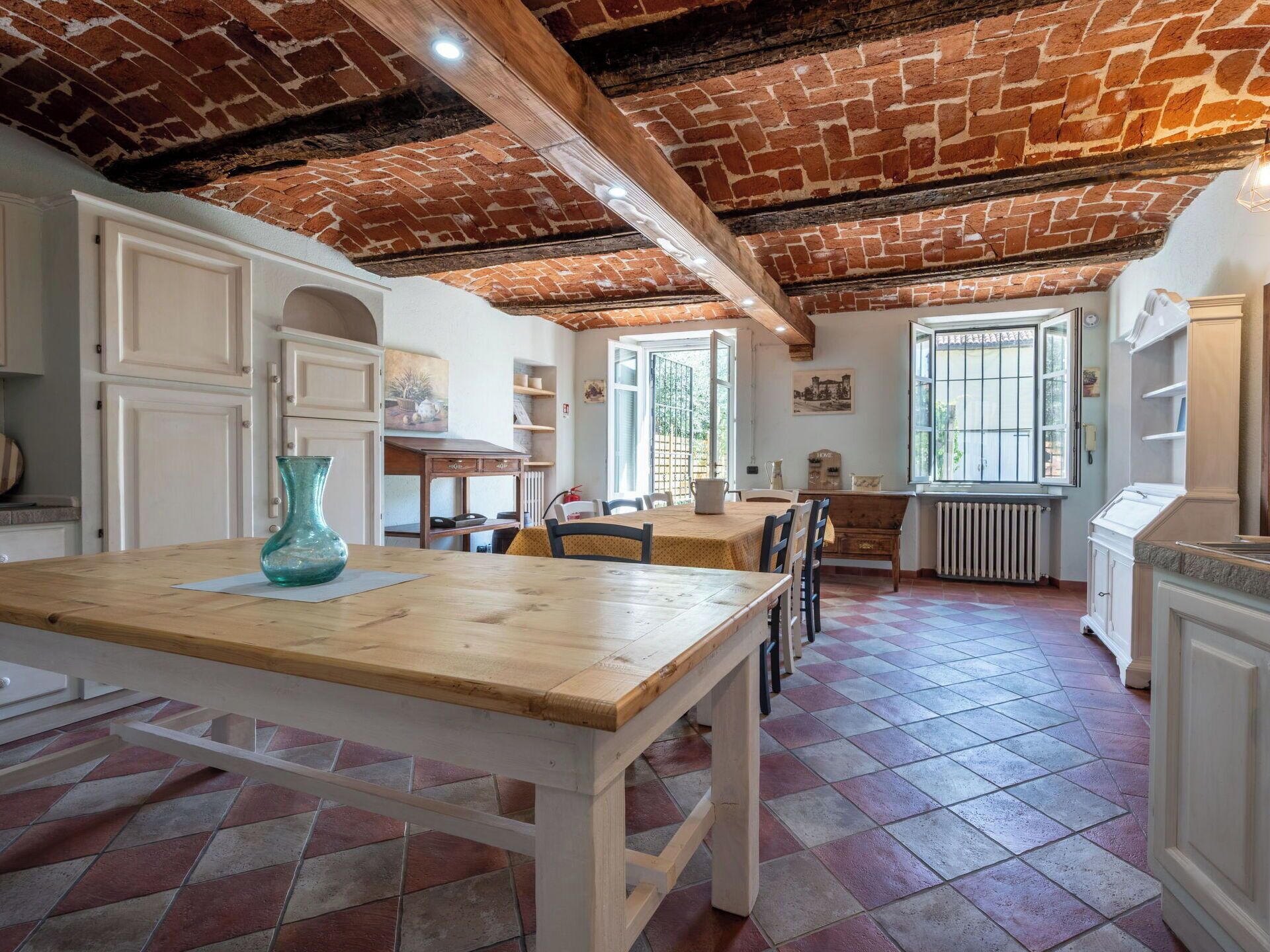 Un coin repas avec une table et des chaises en bois, une cuisine avec des meubles blancs et un plafond en briques.