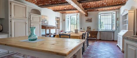 A dining area with a wooden table and chairs, a kitchen with white cabinets, and a brick ceiling.
