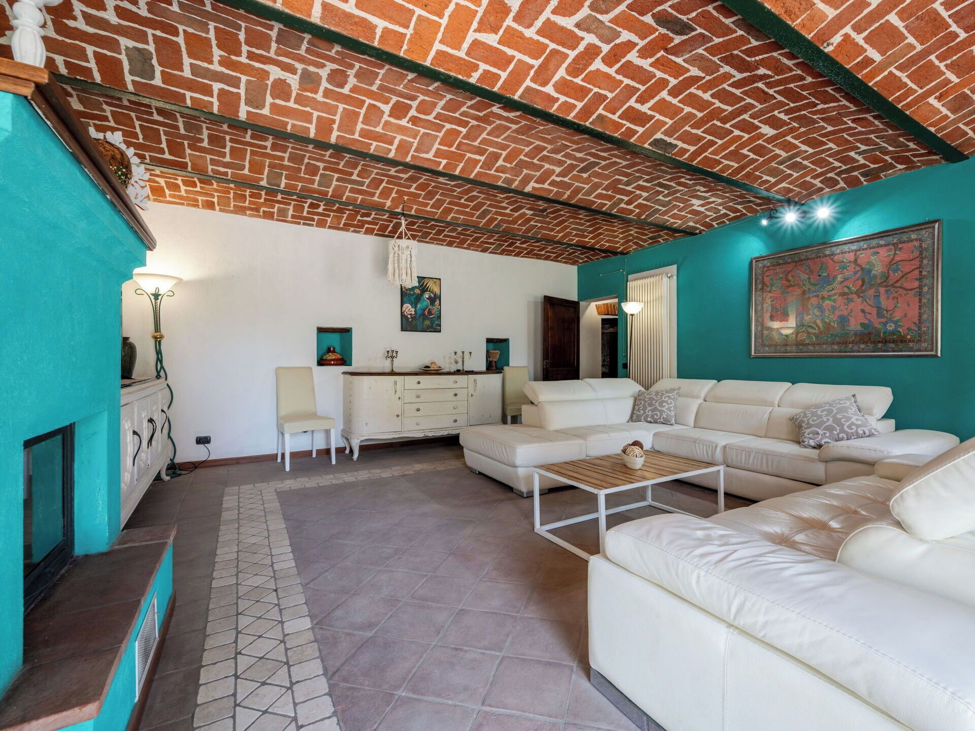 Un salon avec un plafond en briques, un ensemble de canapés blancs, une table basse et un tableau accroché au mur.