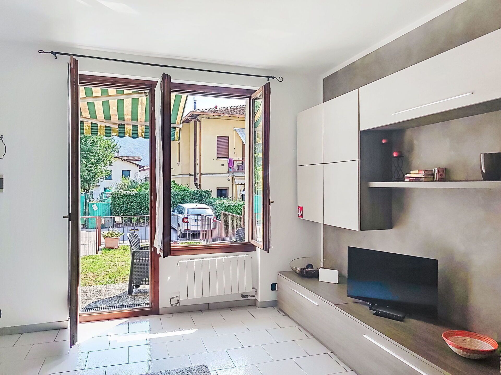 Uma sala de estar moderna com uma televisão grande, um radiador e vista para a rua e edifícios.