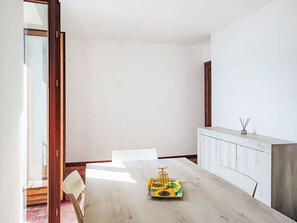 Ein schlichter Essbereich mit einem weißen Tisch, Stühlen und einem Holzschrank.