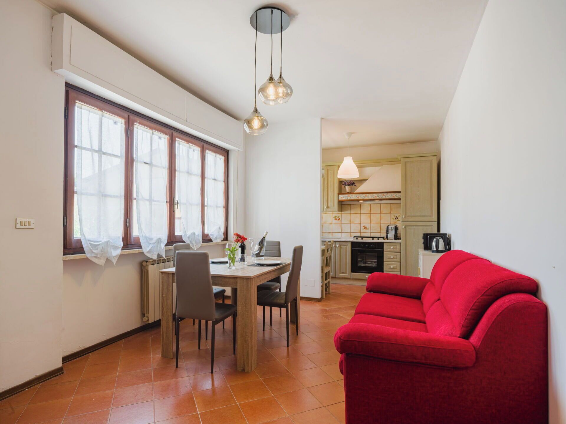 Un coin repas avec une table et des chaises, un canapé rouge et, au fond, une cuisine.