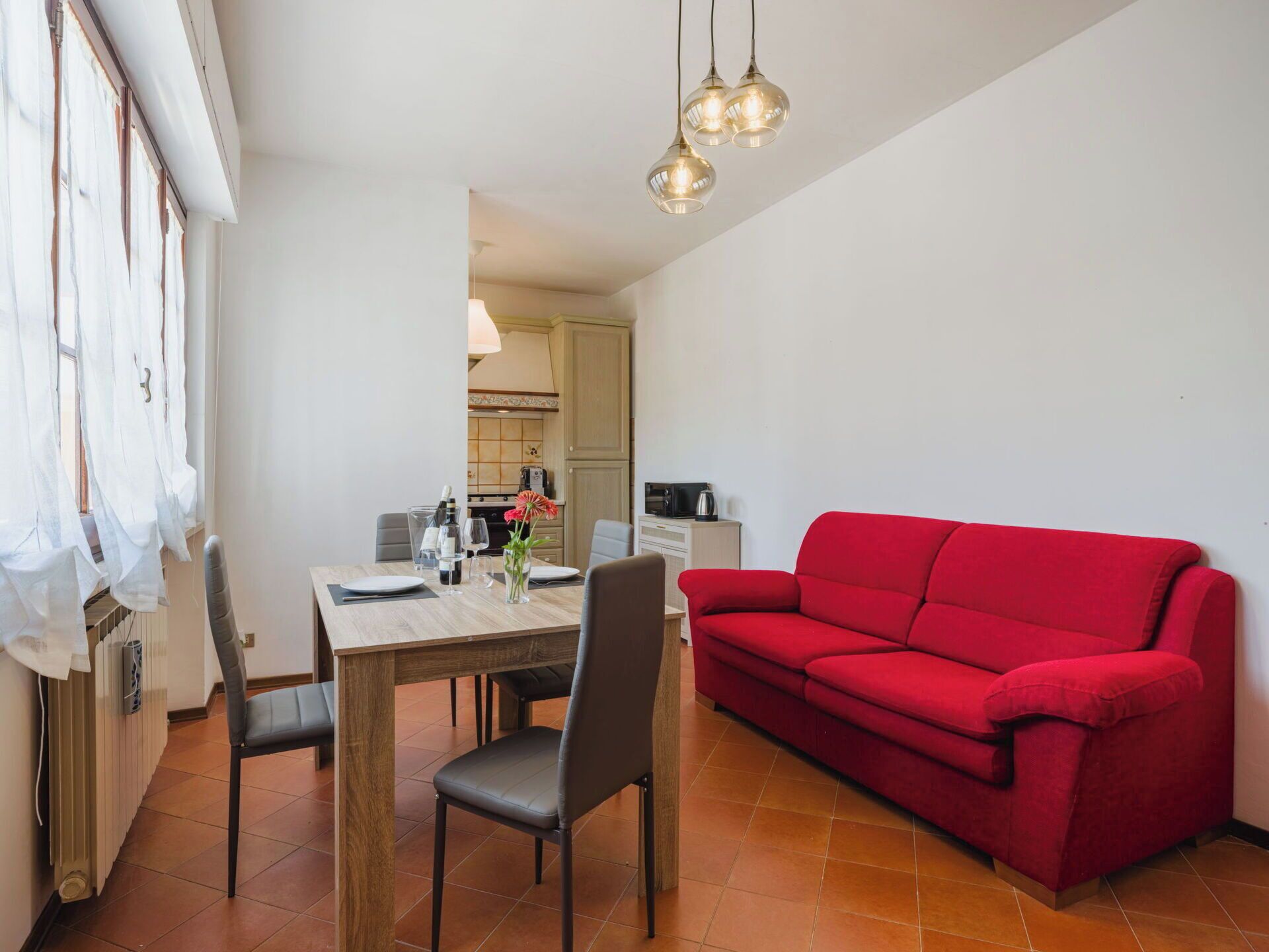 A modern living room with a red sofa, a dining table with chairs, and a kitchen area in the background.