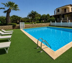 Ein Pool mit Steinrand, umgeben von Kunstgrash und einer Steinmauer.