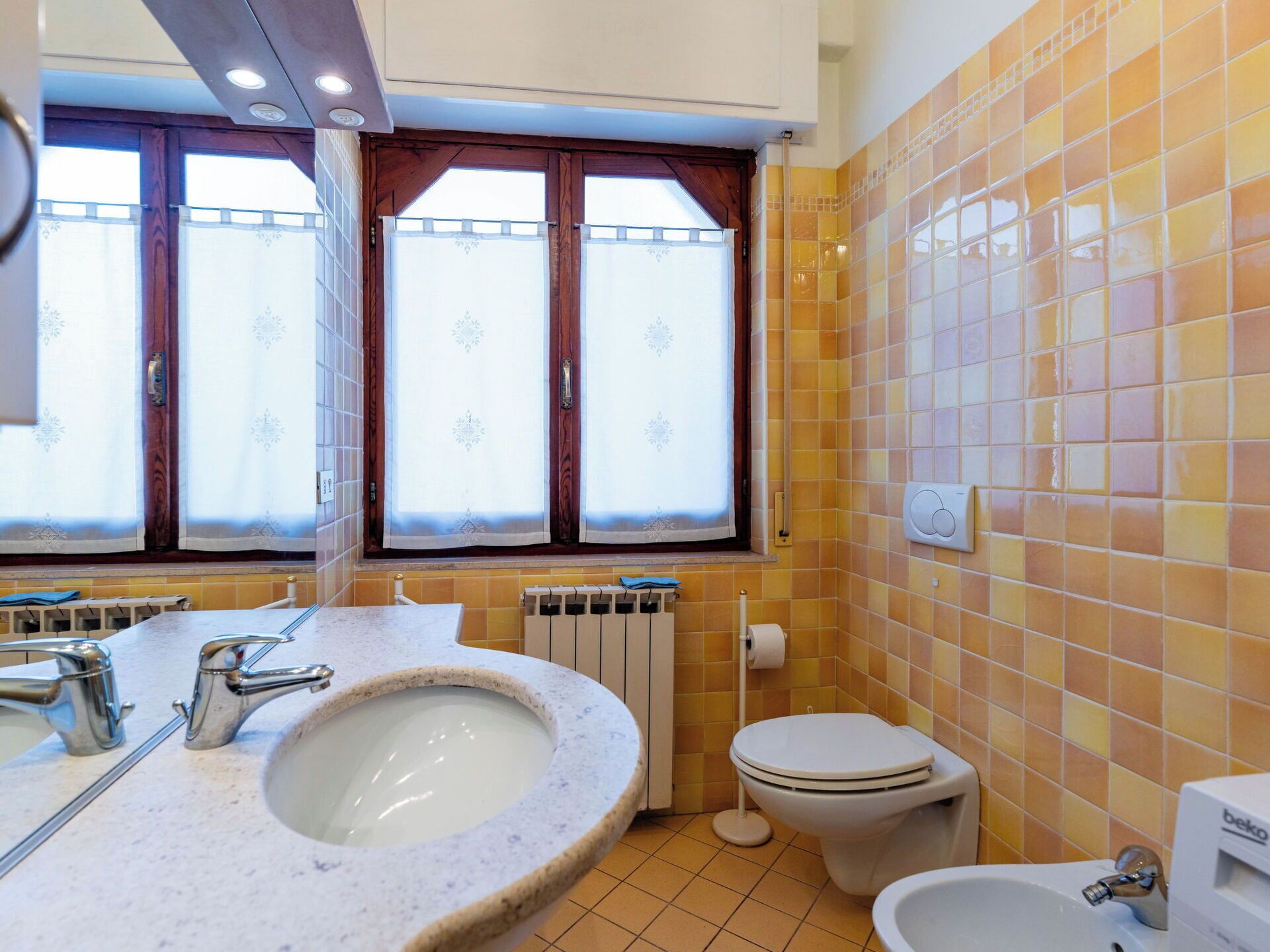 A bathroom with a sink, toilet, bidet, and a window with curtains.