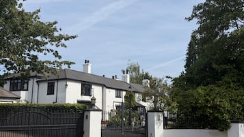 A white building with a gated entrance, surrounded by greenery.