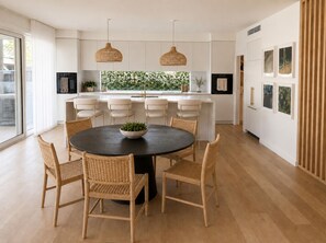 A modern kitchen with a round dining table, wicker chairs, pendant lights, and a view of greenery outside. - Palm Springs Family Home – Gym, Garage, Pets, 10 minutes drive from Manly beach (North Balgowlah)