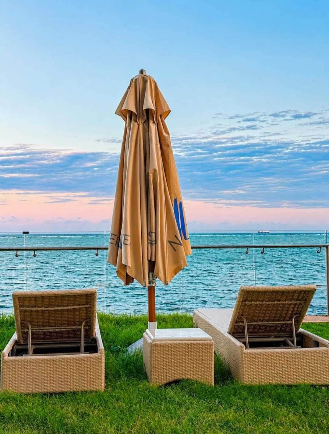 Un área de descanso frente al mar con una sombrilla y dos sillones de mimbre.
