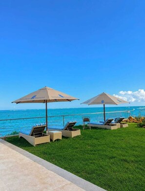 A poolside area with lounge chairs and umbrellas, overlooking a clear blue ocean. - Nyali Luxurious Beachview Apartments  (Mombasa)