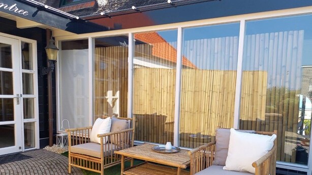 A patio with wicker furniture and a glass door leading to a covered area. - Pura Vida Suite: Enjoy Life! (Oud Ade)
