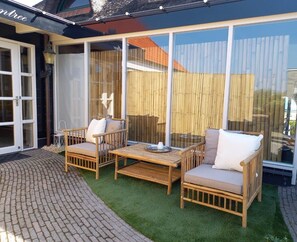 A patio with wicker furniture and a glass door leading to a covered area. - Pura Vida Suite: Enjoy Life! (Oud Ade)