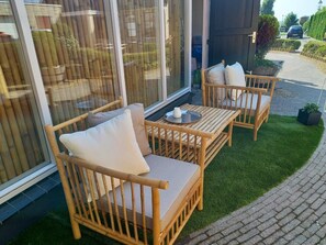 Un espace patio aménagé avec des meubles en osier, comprenant deux chaises et une petite table, et une porte vitrée donnant sur l’intérieur.