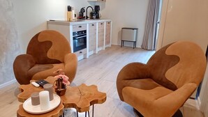 A modern living room with two brown armchairs, a wooden coffee table, and a kitchen in the background. - Pura Vida Suite: Enjoy Life! (Oud Ade)