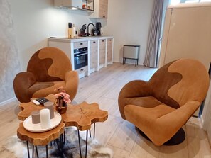 Ein modernes Wohnzimmer mit zwei braunen Sesseln, einem Holztisch und einer Küche im Hintergrund.