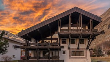 Ein Chalet mit Holzbalkon, großen Fenstern und einer Bergkulisse.