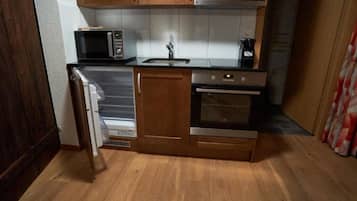 Eine kompakte Küche mit Holzschränken, einer Mikrowelle, einem Spülbecken und einem Herd.