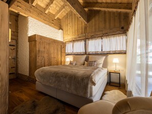 Ein Schlafzimmer einer Holzhütte mit einem großen Bett, einem Nachttisch und einem Fenster mit Vorhängen.