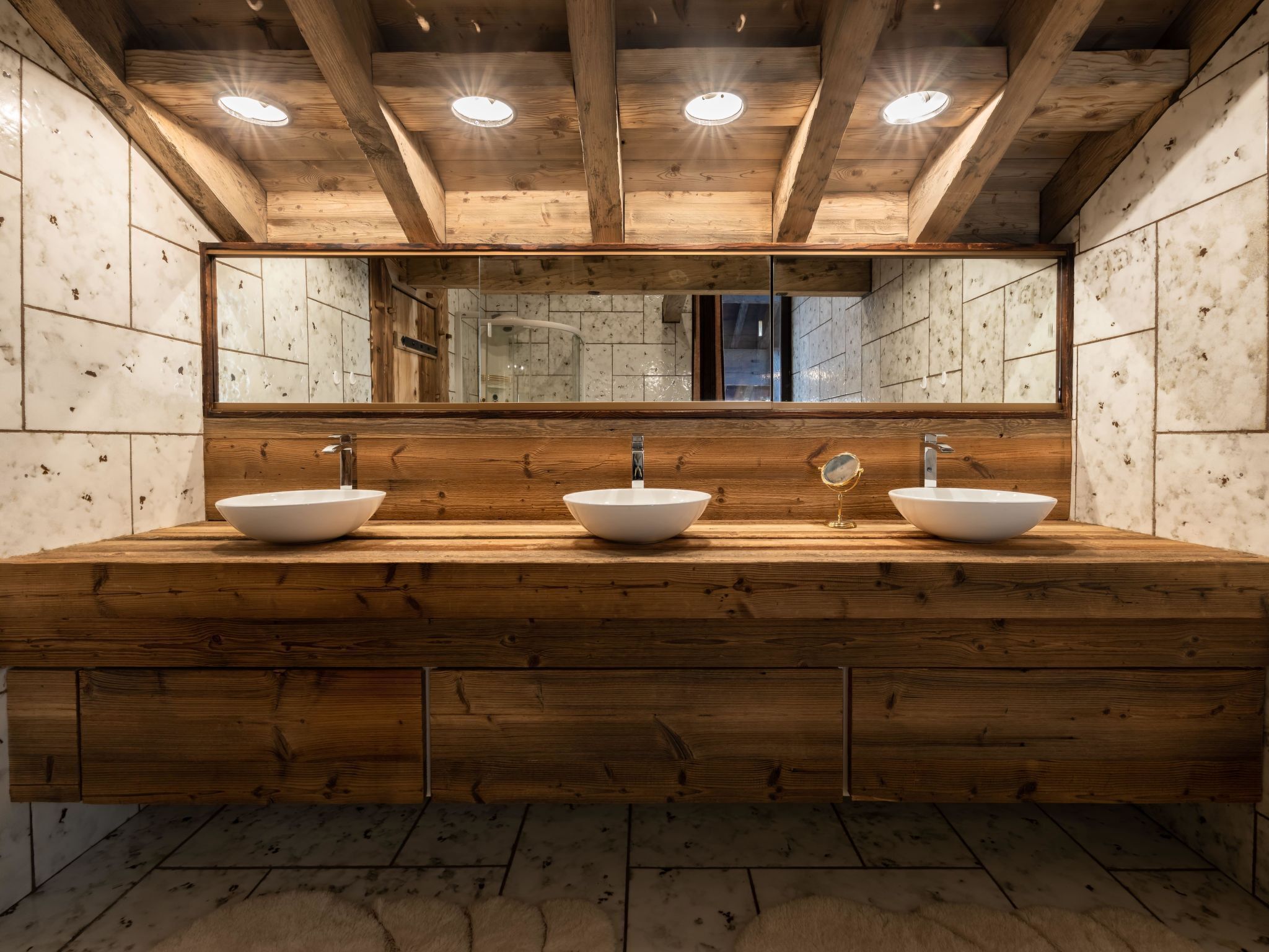 A wooden vanity with three sinks and a large mirror above.