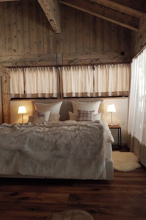 Ein gemütliches Schlafzimmer mit einem großen Bett, Holzbalkendecke und zwei Nachttischlampen.