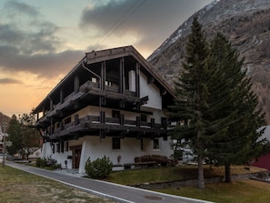 Ein mehrstöckiges Gebäude mit einer hölzernen Balkonkonstruktion, umgeben von Bäumen und einem Berg im Hintergrund.