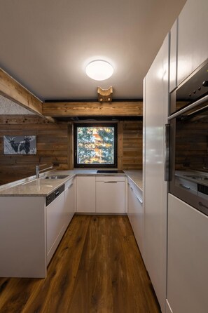Eine moderne Küche mit Holzboden, einem Fenster mit Blick auf Bäume und einem eingebauten Geschirrspüler.