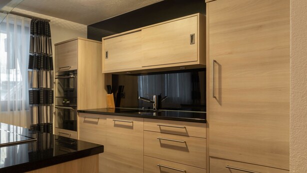 A modern kitchen with wooden cabinets, a black countertop, and stainless steel appliances. - Villa Alpenhof Appartement/Fewo Wohnung für 6 Personen by Interhome (Saas-Almagell)