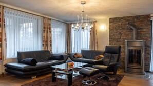 A modern living room with a sofa set, a glass coffee table, a chandelier, and a stone wall with a fireplace. - Villa Alpenhof Appartement/Fewo Wohnung für 6 Personen by Interhome (Saas-Almagell)