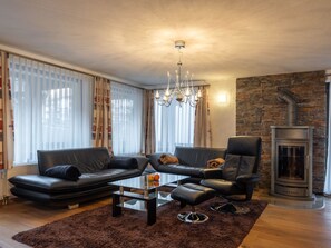 A modern living room with a sofa set, a glass coffee table, a chandelier, and a stone wall with a fireplace. - Villa Alpenhof Appartement/Fewo Wohnung für 6 Personen by Interhome (Saas-Almagell)