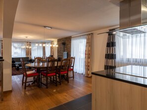 A modern kitchen with a central island, a dining area with wooden chairs and a round table, and a stone fireplace. - Villa Alpenhof Appartement/Fewo Wohnung für 6 Personen by Interhome (Saas-Almagell)