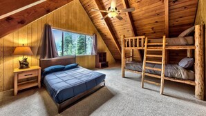 A cozy attic bedroom with a bunk bed, a single bed, a window with a view of trees, and a ceiling fan. - Tahoe River Chalet 2782b 4 Bedroom Home (South Lake Tahoe)